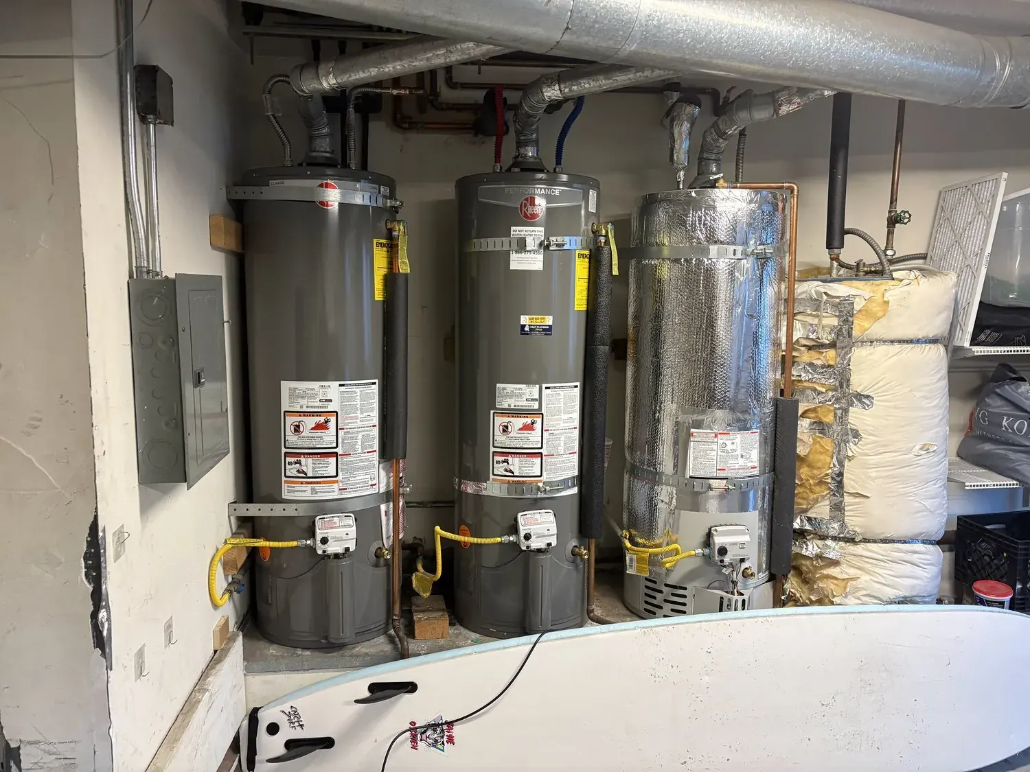 Three residential water heaters with insulation and piping in utility room installation